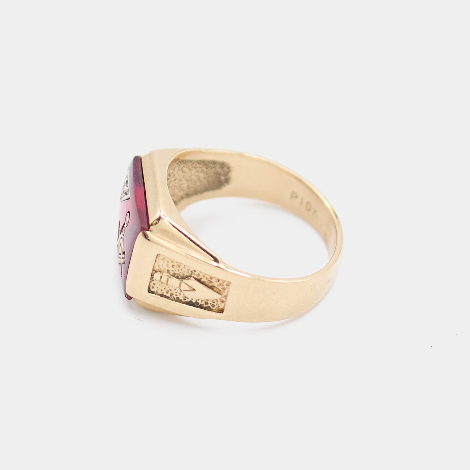 Side profile of a pre-owned 10K yellow gold Freemason ring showing the textured engraved shoulder detail, red center stone, and 10K hallmark stamp inside the band. Size 9.5.