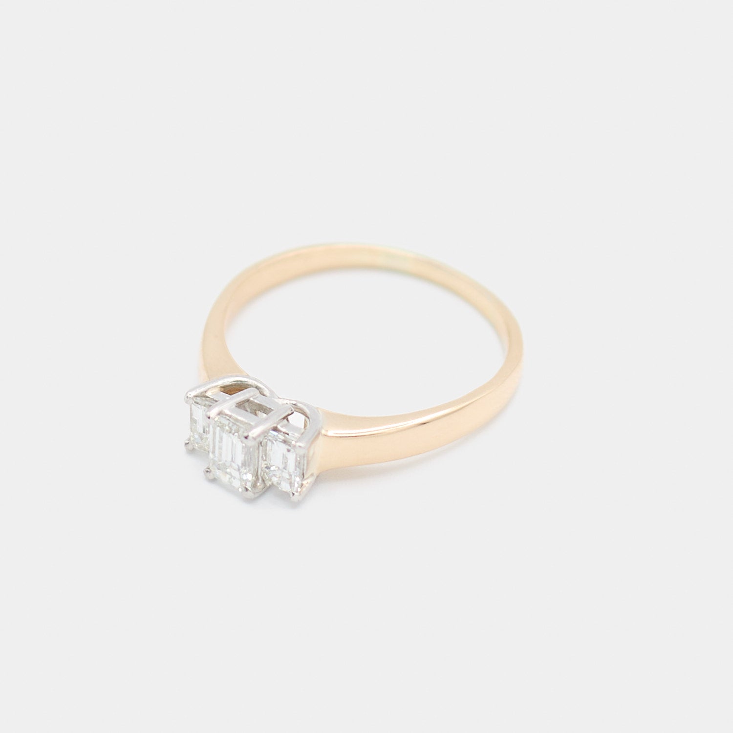 Angled 3/4 view of a pre-owned 14K yellow gold engagement ring showing the three emerald cut diamonds and prong setting detail.