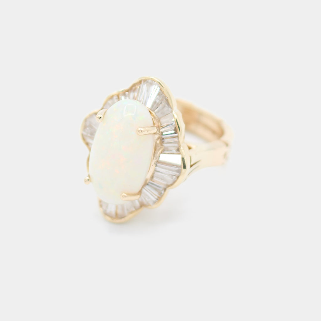 Angled 3/4 view of a pre-owned 14K yellow gold ring featuring an oval cabochon opal surrounded by a scalloped baguette diamond halo.
