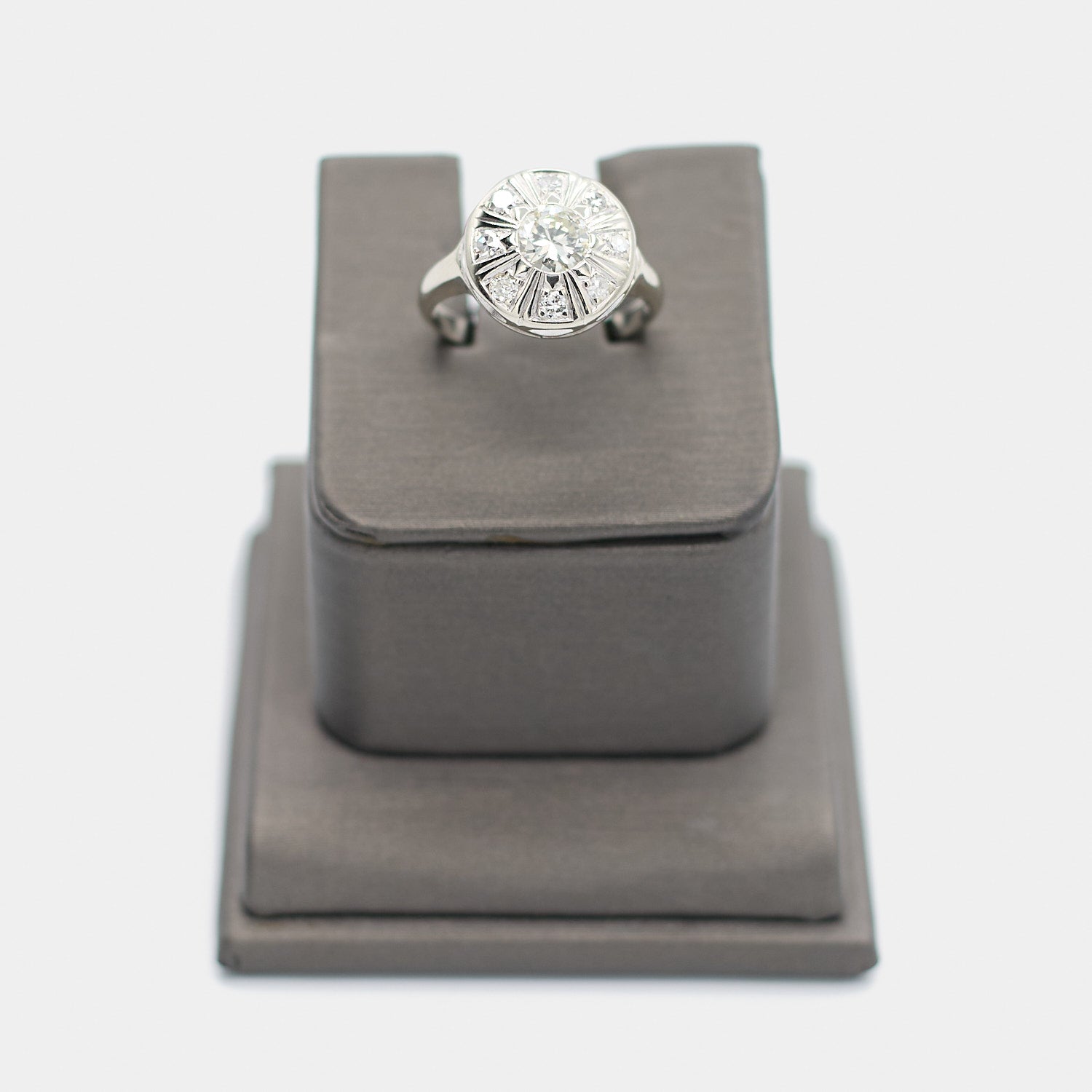Pre-owned 14K white gold Art Deco diamond ring, size 5.75, featuring a round center diamond surrounded by 8 smaller diamonds in a sunburst pattern, shown front-facing on a display stand.