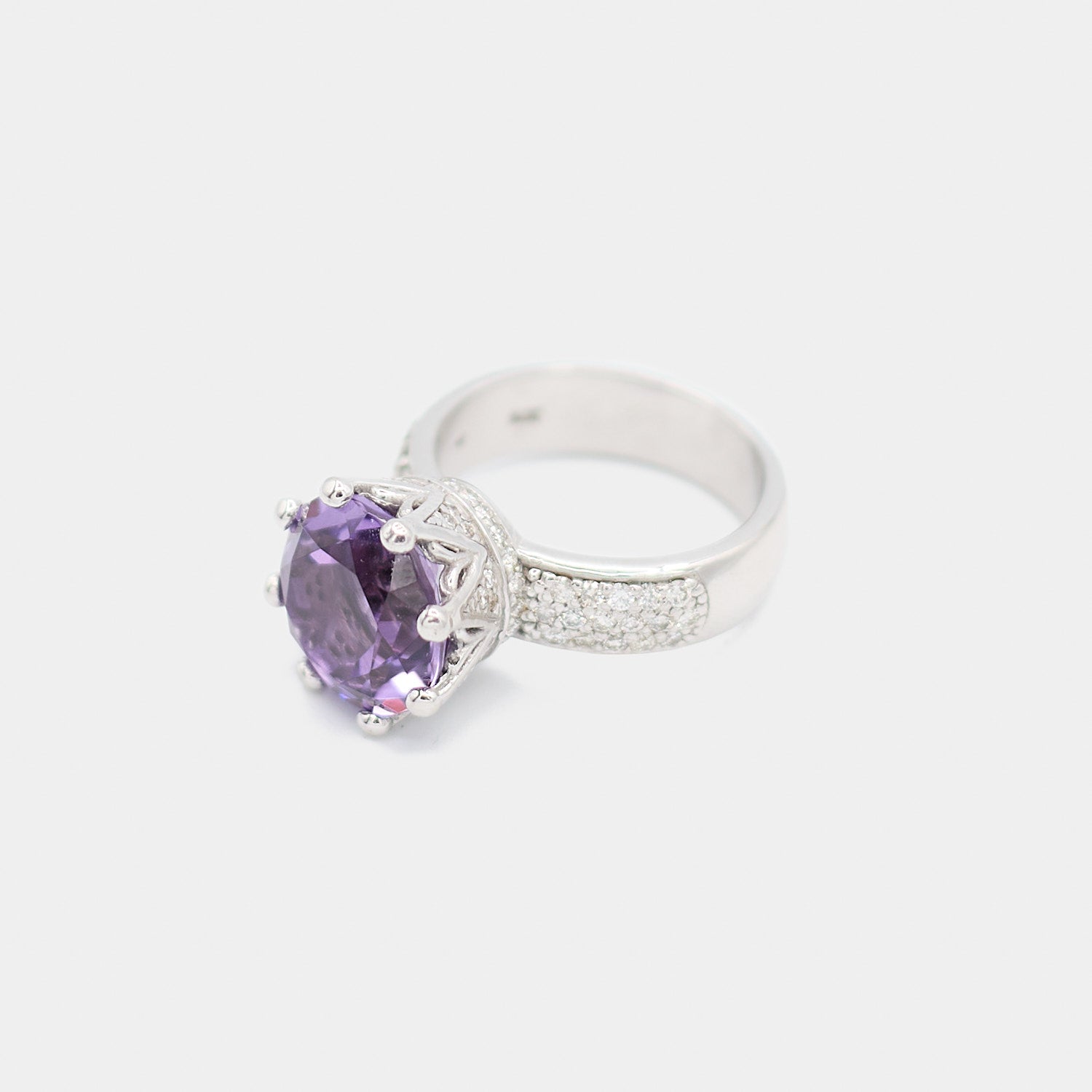 Angled view of a pre-owned 14K white gold ring featuring a round purple stone in a crown style setting with diamond chip pave accents on the band, weighing 10.67 grams.
