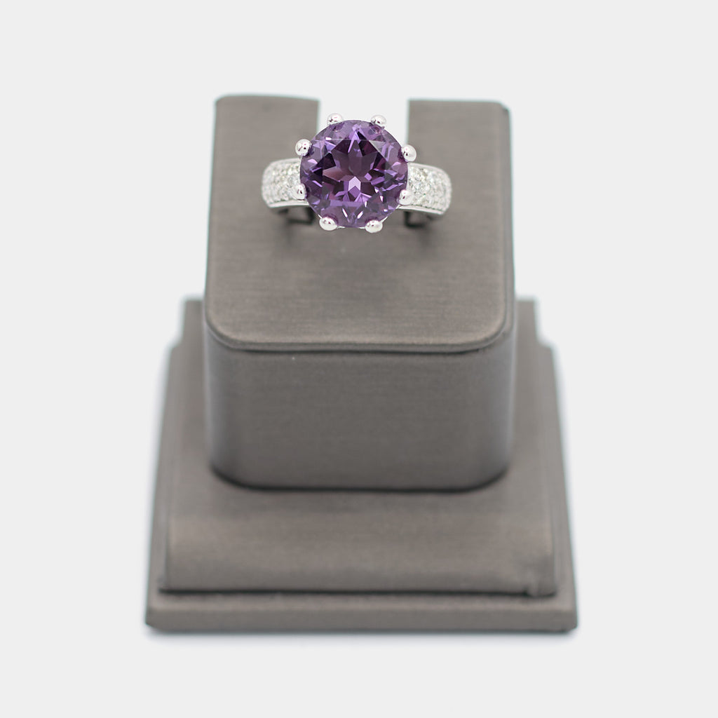 Pre-owned 14K white gold ring with a large round purple center stone in a crown prong setting, accented by pave diamond chips along the shoulders. Size 7.25, shown front-facing on a display stand.