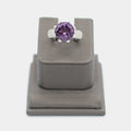 Pre-owned 14K white gold ring with a large round purple center stone in a crown prong setting, accented by pave diamond chips along the shoulders. Size 7.25, shown front-facing on a display stand.