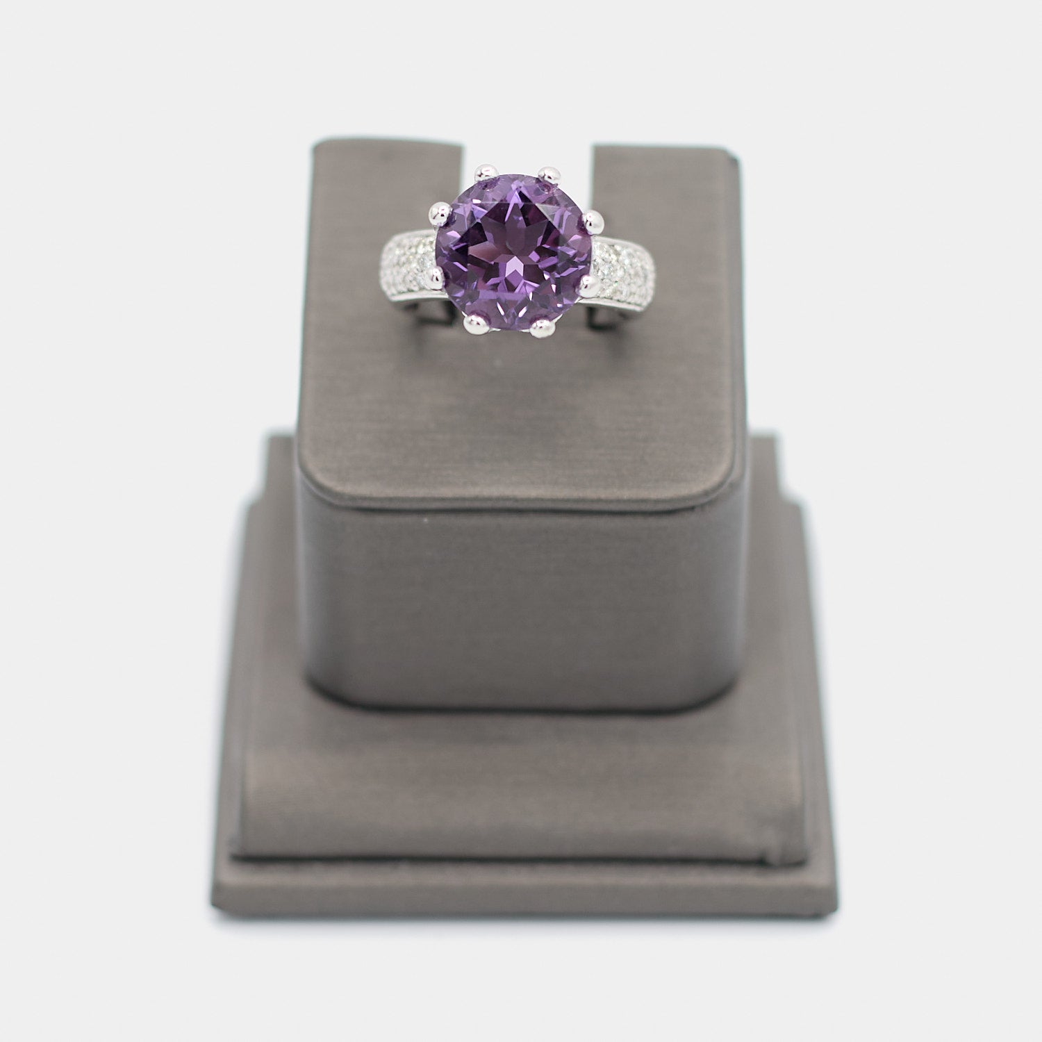 Pre-owned 14K white gold ring with a large round purple center stone in a crown prong setting, accented by pave diamond chips along the shoulders. Size 7.25, shown front-facing on a display stand.