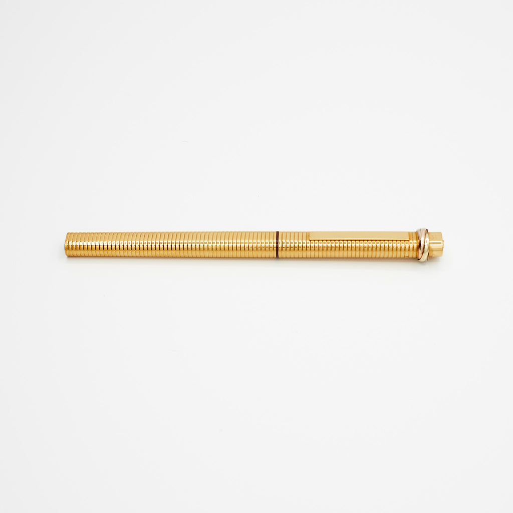 Gold-plated vintage Cartier ballpoint pen resting on a white background, side view.