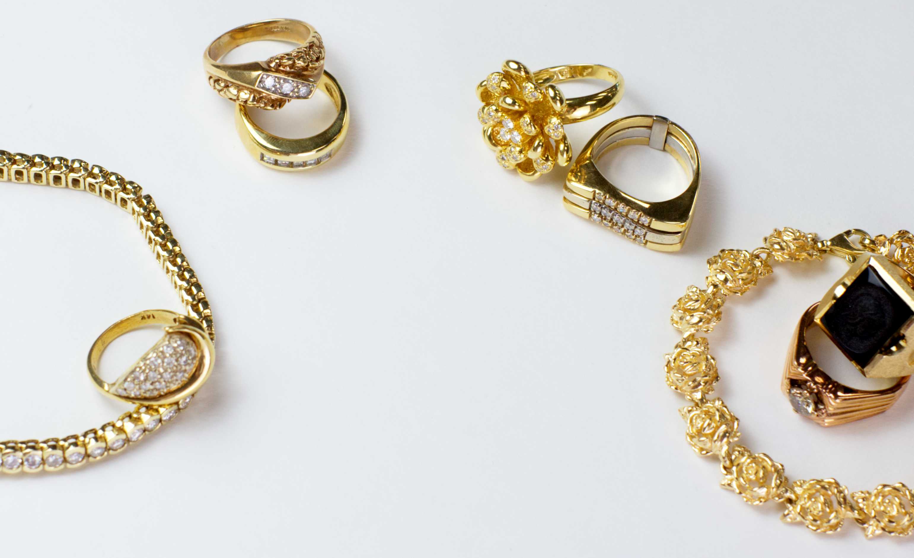 Gold jewelry photographed on a white background showcasing several rings and bracelets