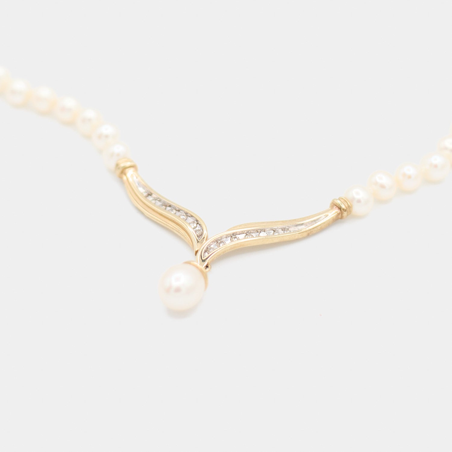 Angled close-up of a pre-owned pearl necklace showing the dangling pearl drop and diamond set gold centerpiece from the side.