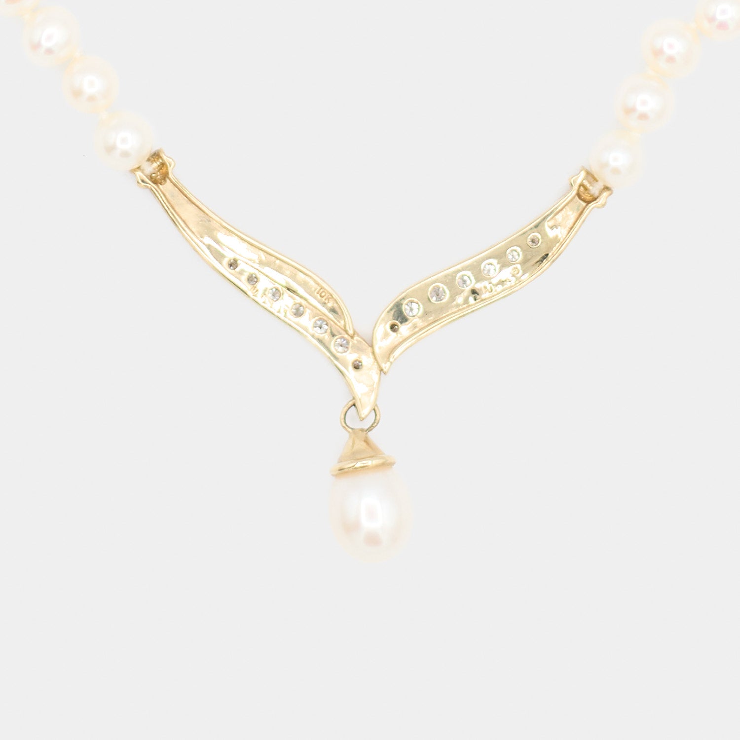 Close-up back view of a pre-owned pearl necklace's 10K gold centerpiece, showing the diamond settings and 10K hallmark stamp. 