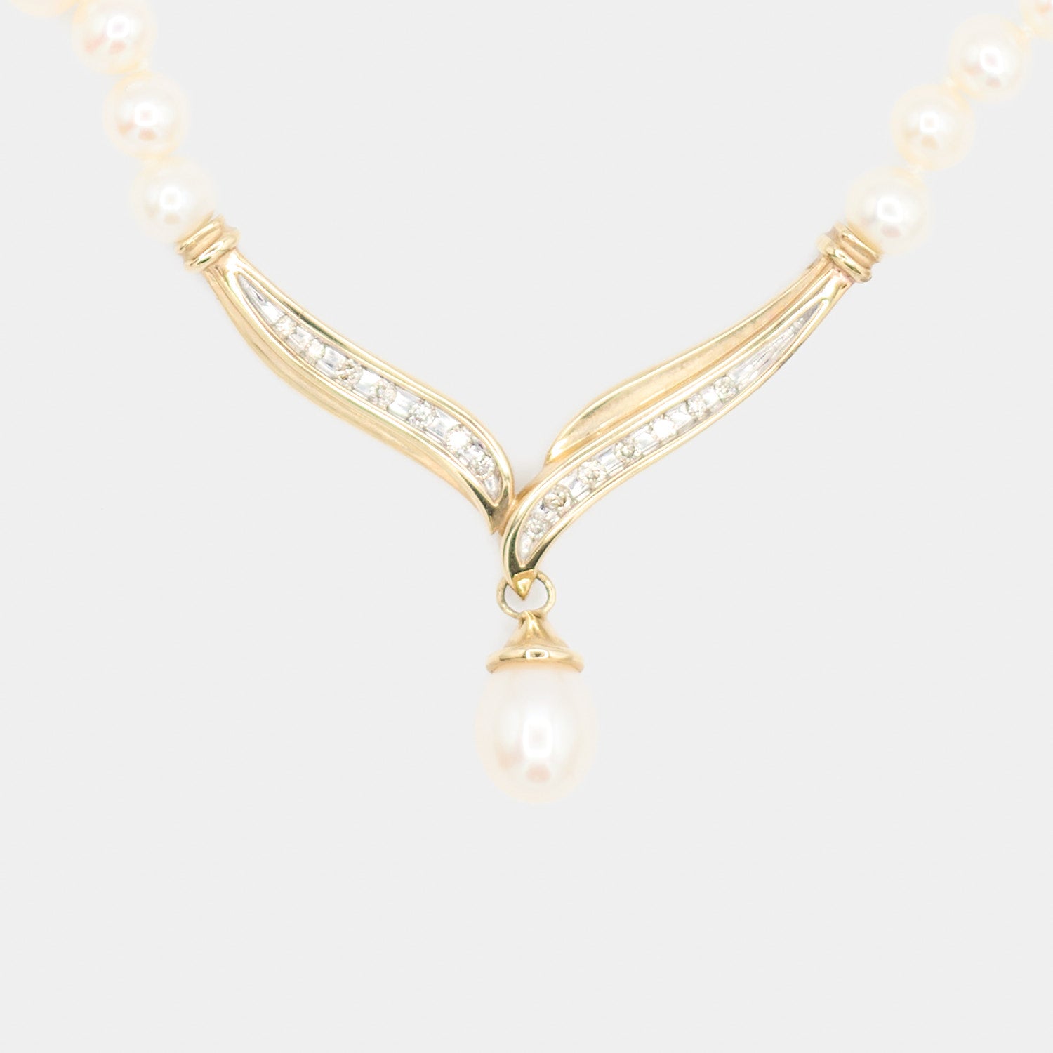 Close-up front view of a pre-owned pearl necklace's 10K gold centerpiece, showing the V-shaped diamond design and dangling pearl drop.