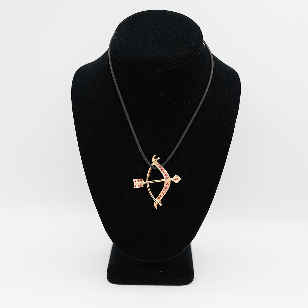Verified pre-owned 14K gold bow and arrow pendant, set with 19 red stones, 2 inches long, displayed on a black mannequin for scale.