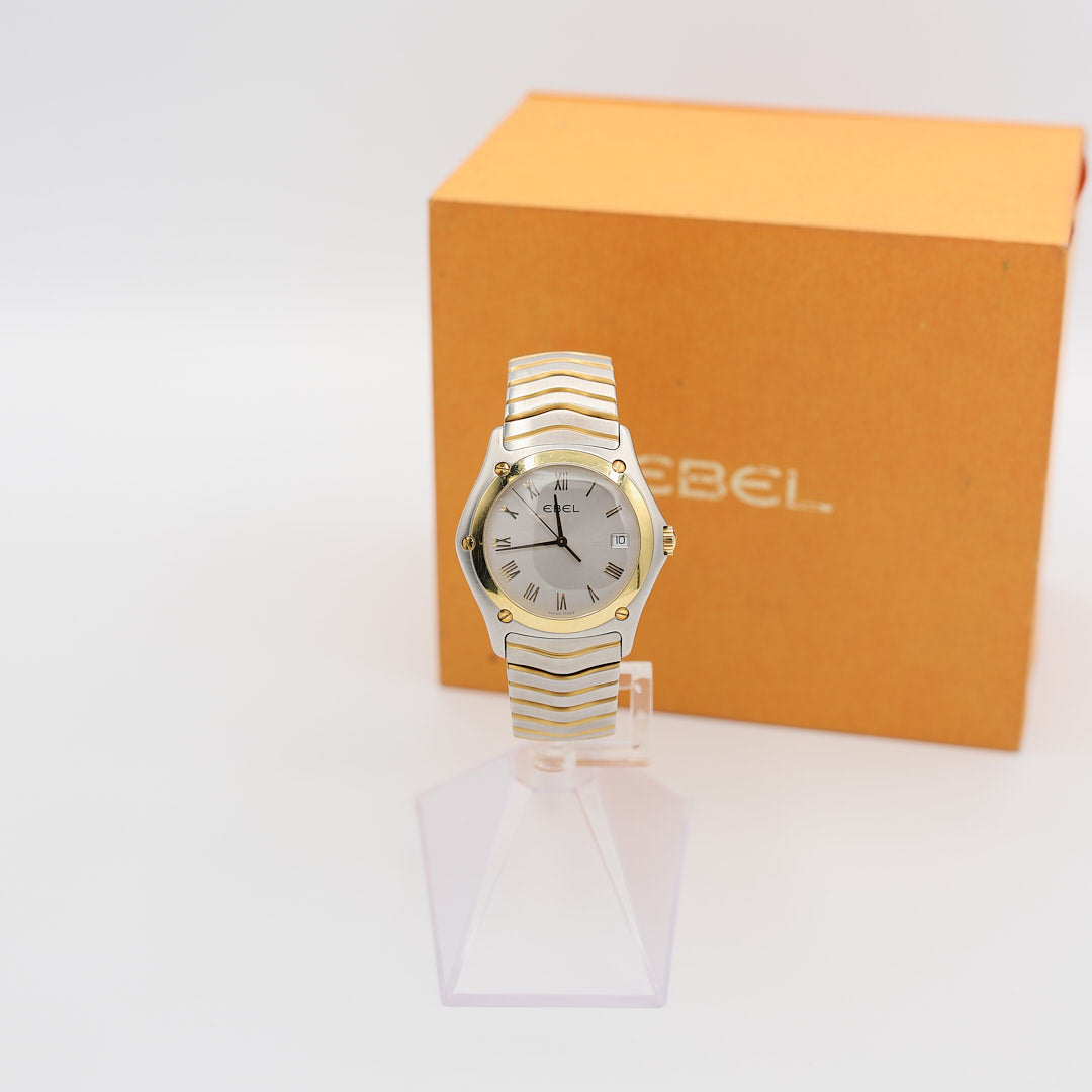 Front view of the Ebel Classic Wave 18K gold and stainless steel watch, displayed next to the original presentation case box.