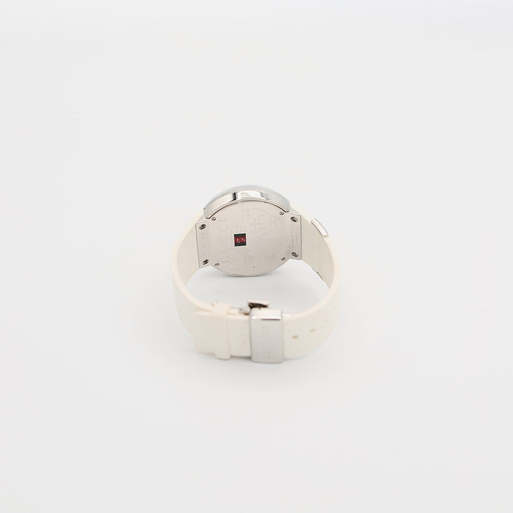 Back view of the Gucci 114-2 stainless steel watch standing up, highlighting the case back and the contrast of the white rubber wristband and 64.06 gram weight.