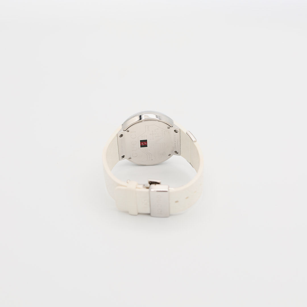 Back view of the Gucci 114-2 stainless steel watch standing up, highlighting the case back and the contrast of the white rubber wristband and 64.06 gram weight.